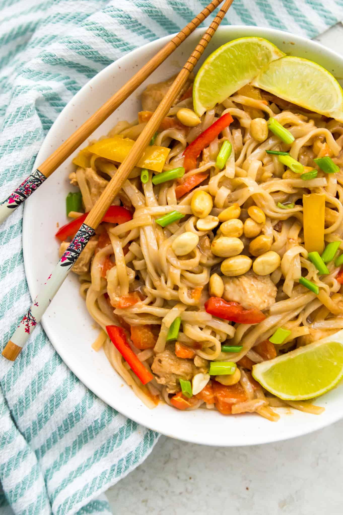 A bowl of Instant Pot Pad Thai garnished with lime wedges and peanuts. 