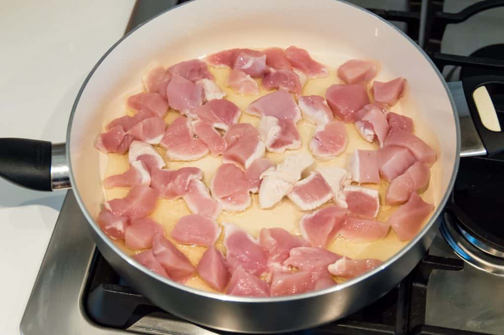 Chopped chicken pieces cooking in a pan on the stovetop.