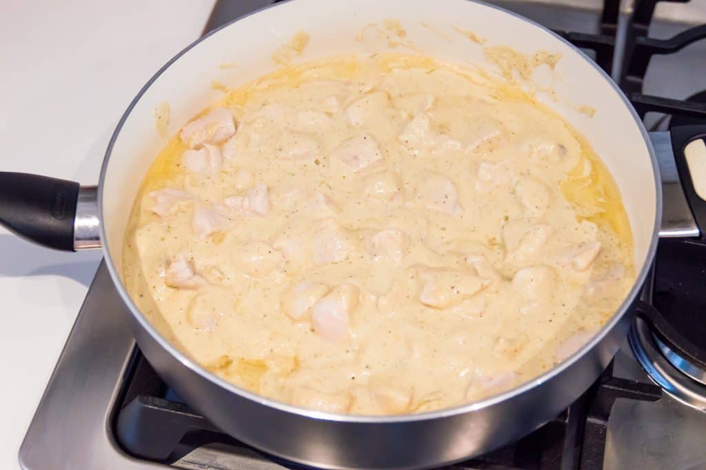 Cooked chicken pieces in Alfredo Sauce in a pan on the stovetop.