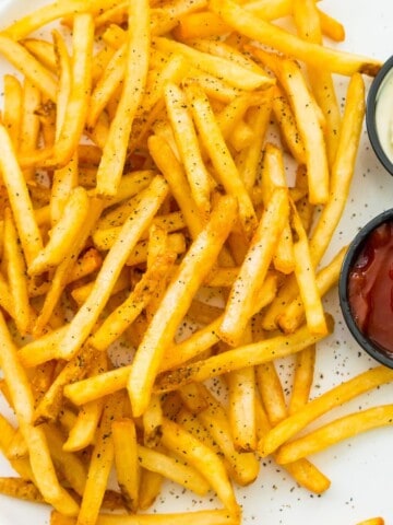 A plate of cooked French fries with sides of ketchup and mayonnaise.
