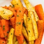 A plate full of honey glazed carrots and parsnips topped with fresh thyme.