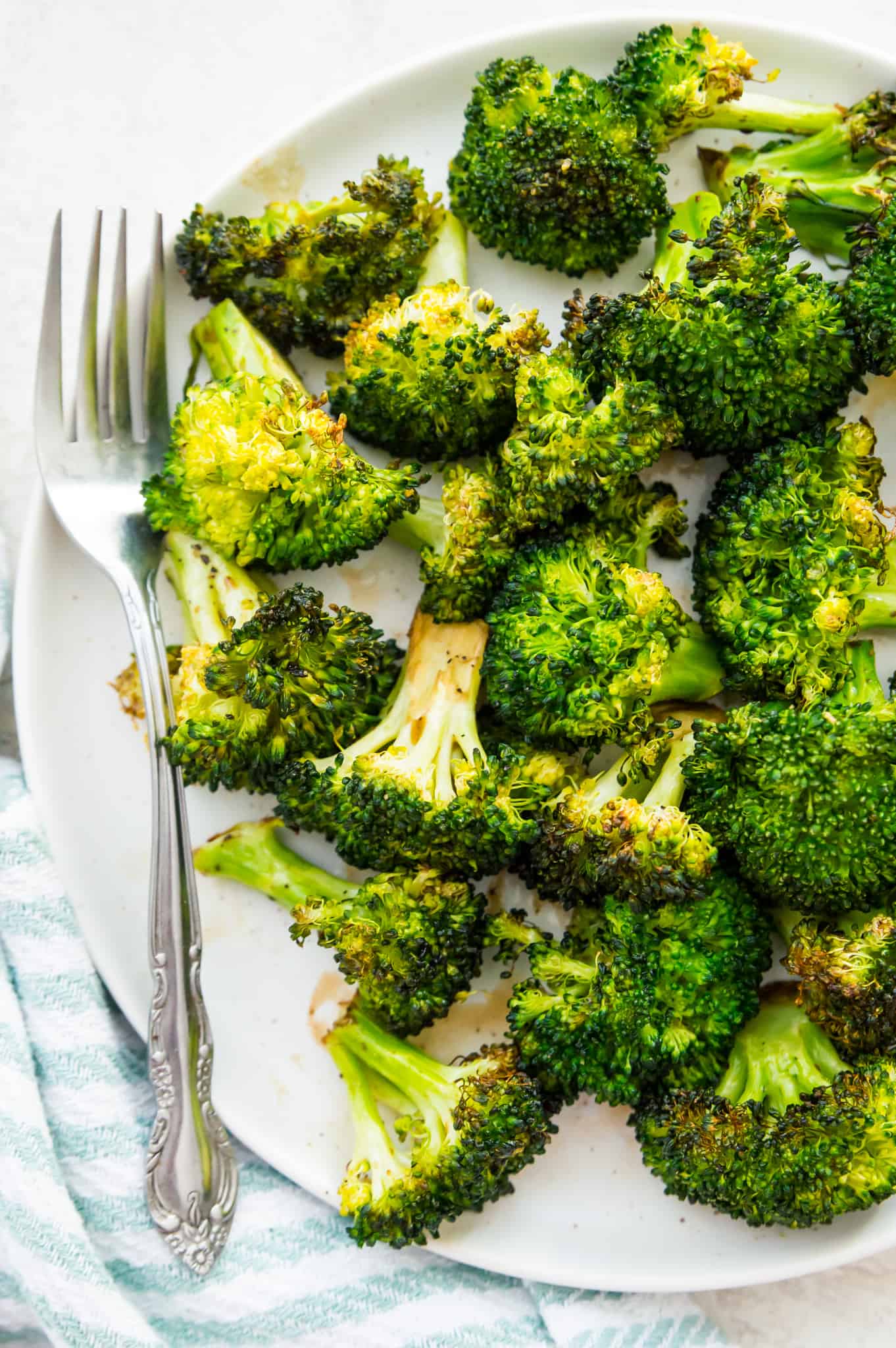 A plate of cooked broccoli with a fork beside the broccoli 