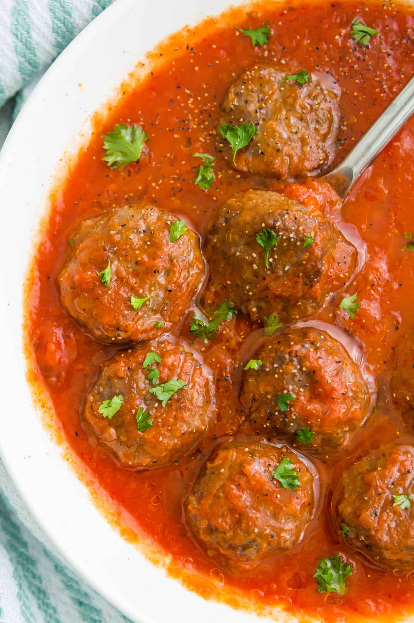 A bowl of cooked meatballs in tomato sauce, garnished with fresh parsley.