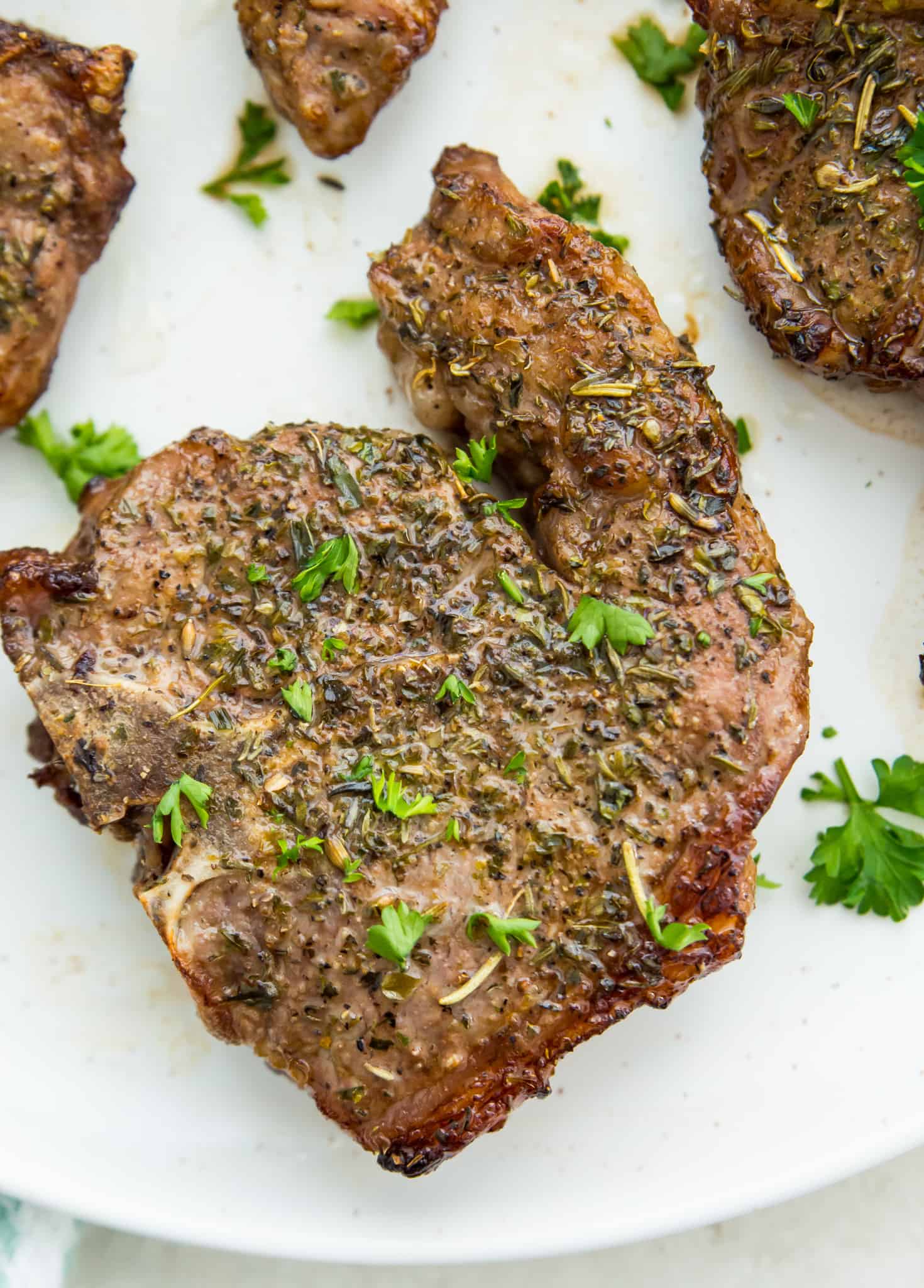 A cooked lamb chop on a plate with fresh parsley as garnish.