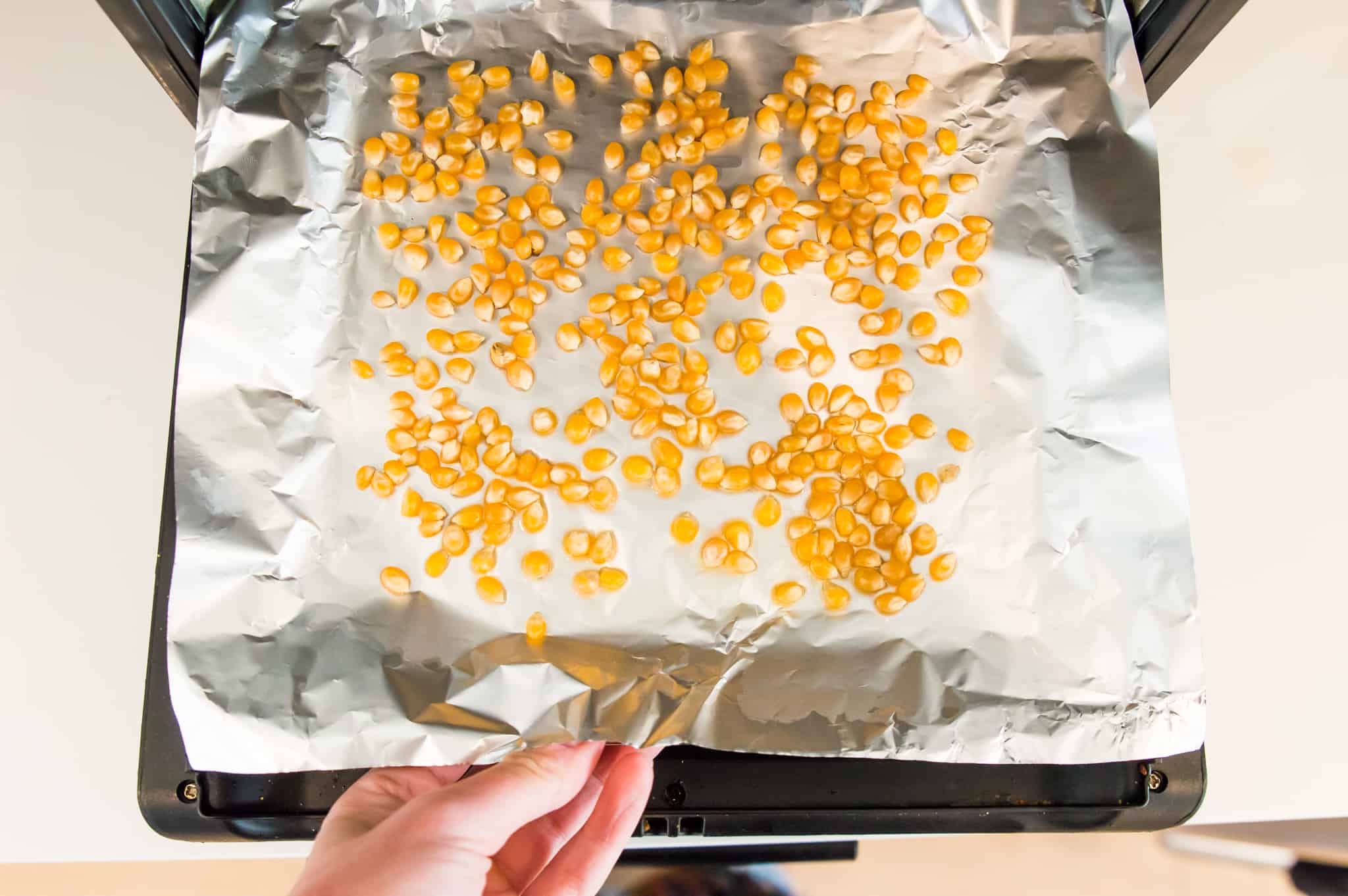 An air fryer tray lined with tinfoil with popcorn kernels on it.