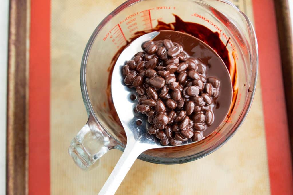 Chocolate covered espresso beans being scooped out of a measuring cup.