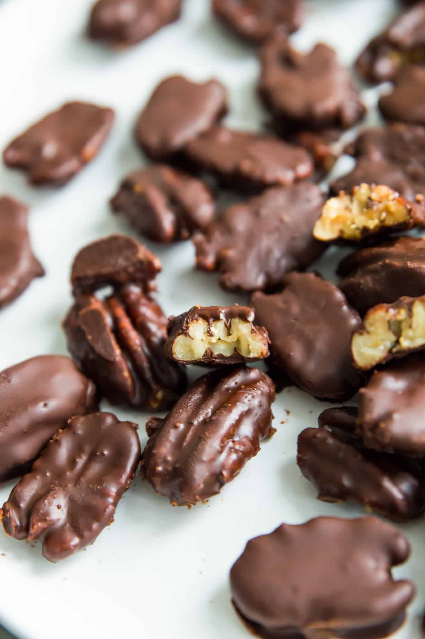 A plate of chocolate covered pecans, with a bite out of one of them.