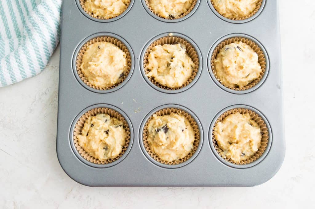 A muffin tray with parchment paper muffin cups in it and batter in the muffin cups. 