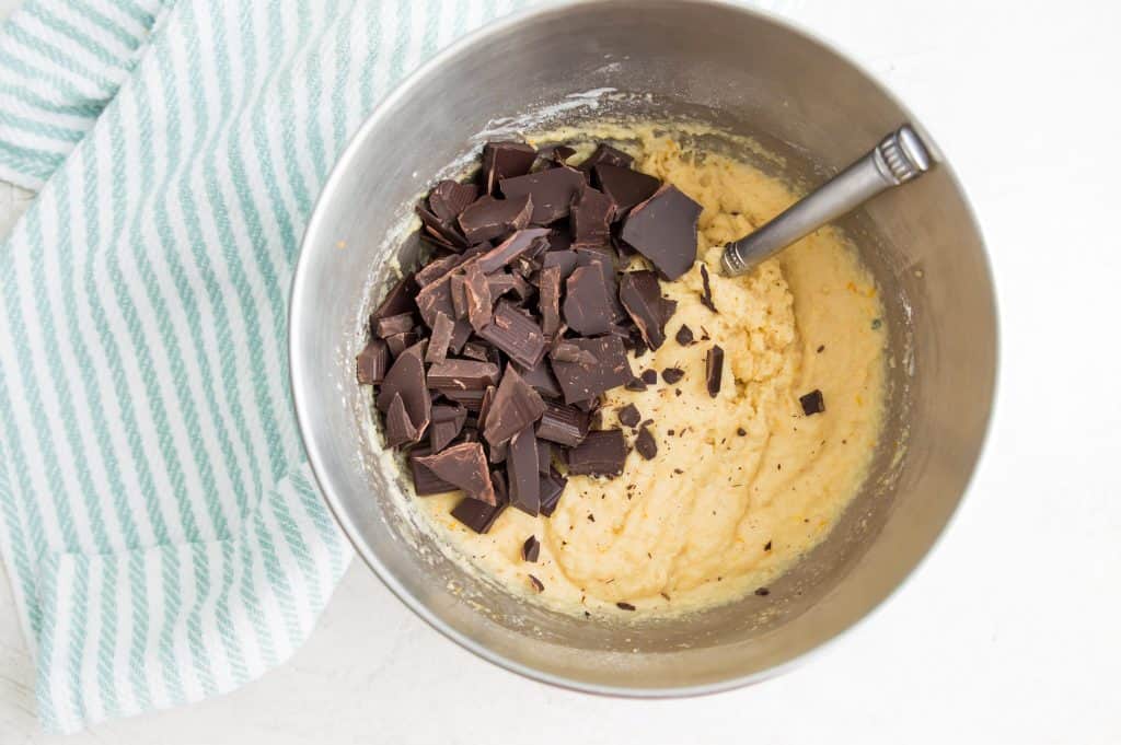 Muffin batter in a large bowl with pieces of broken chocolate on it and a spoon in the bowl.