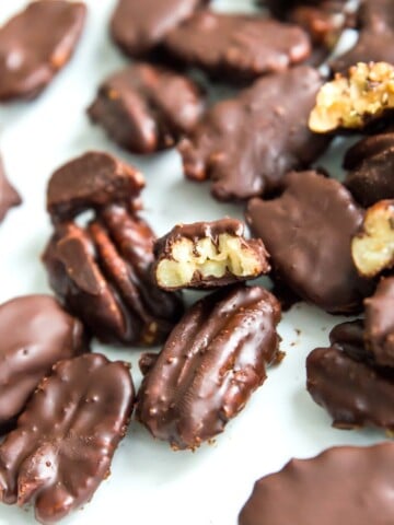 Chocolate covered pecans on a plate with one with a bite out of it.