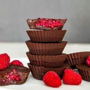 A stack of five chocolate raspberry cups and the top one has a bite out of it so you can see the raspberry filling.