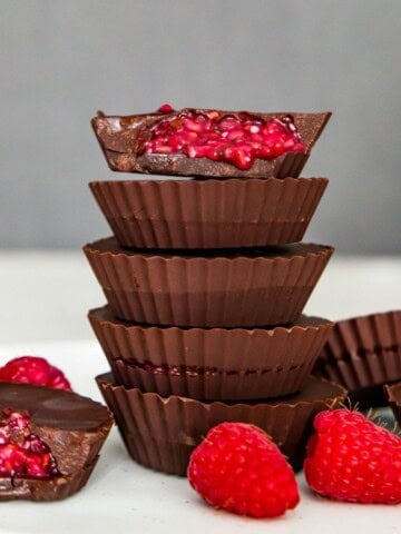 A stack of five chocolate raspberry cups and the top one has a bite out of it so you can see the raspberry filling.