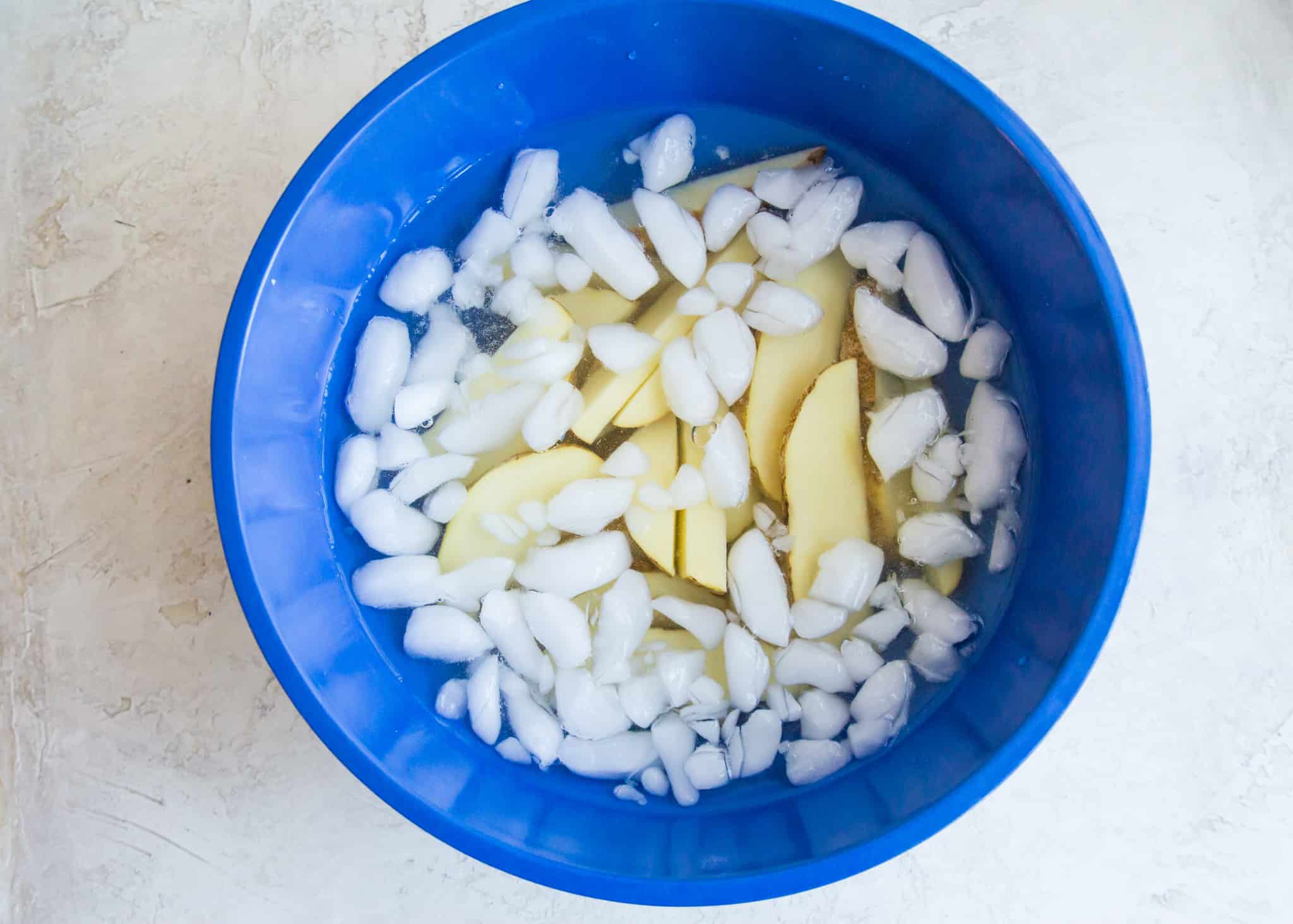 Potato wedges soaking in a bowl of ice water.