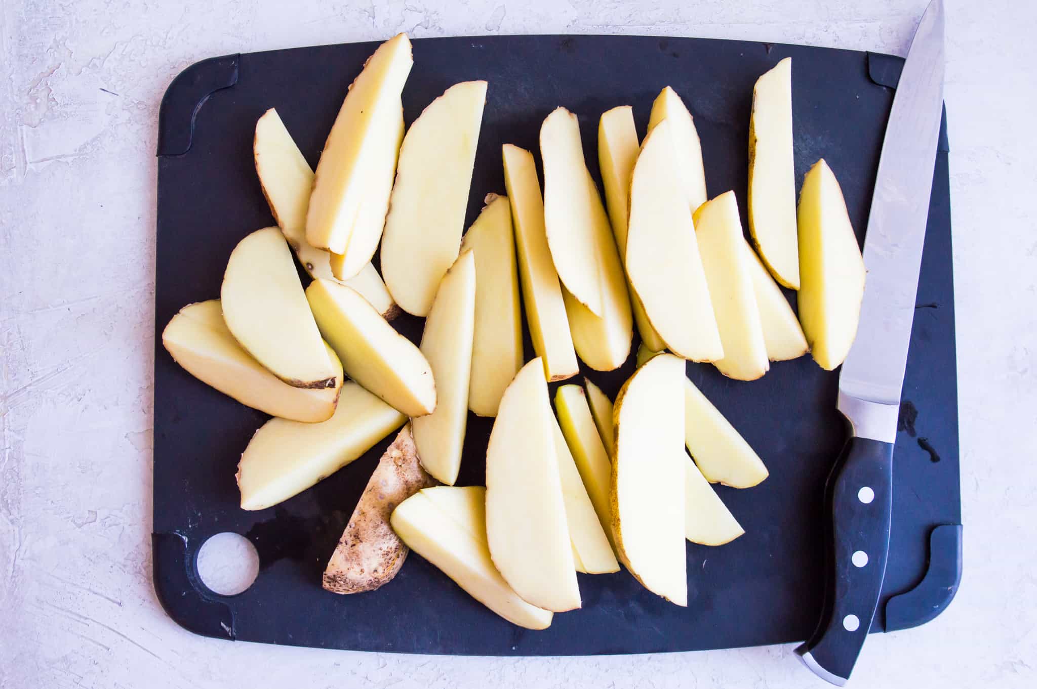 Chopped potatoes on a cutting board with a knife beside them.