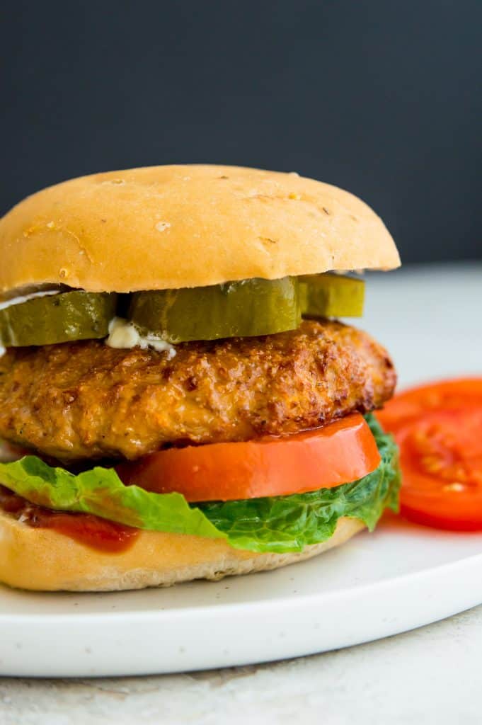 A turkey burger cooked in an air fryer on a plate with pickles, tomatoes and potato chips