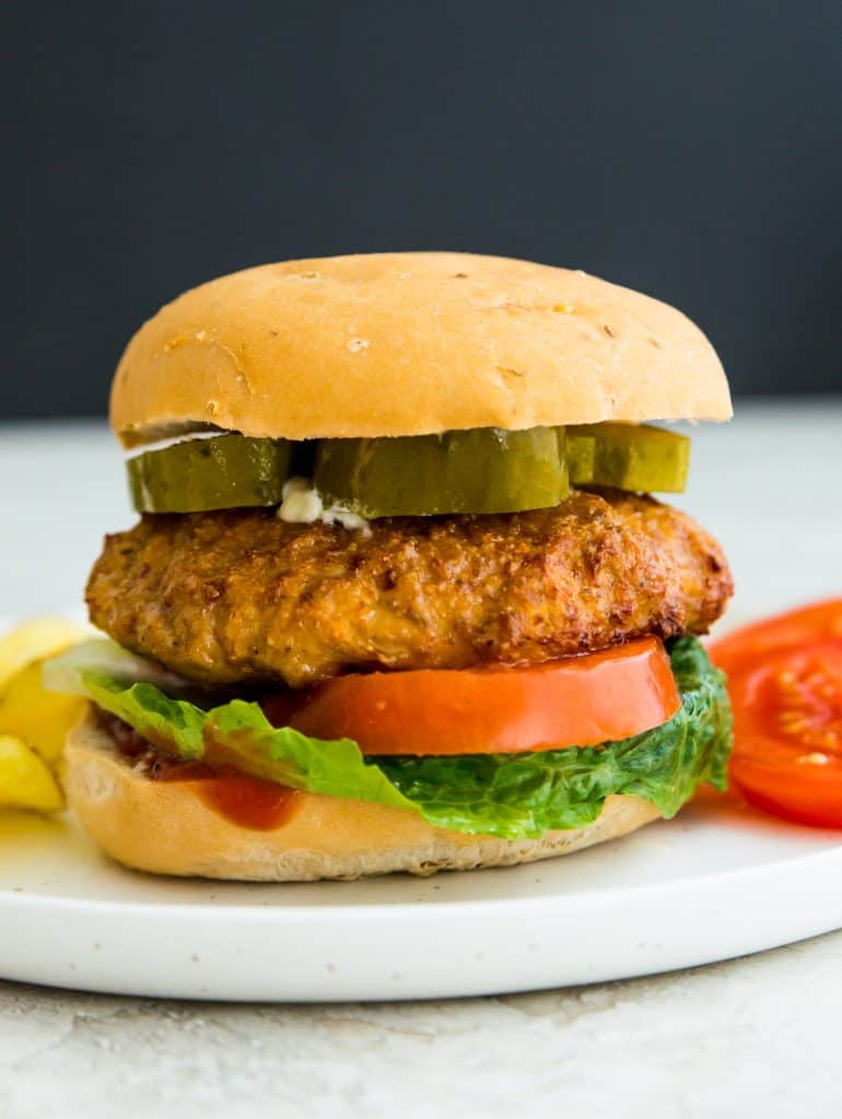 An air fryer turkey burger on a bun on a plate with tomatoes and chips
