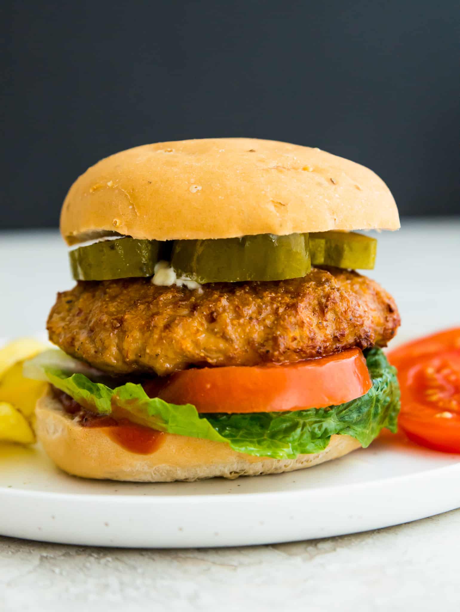 An air fryer turkey burger on a bun on a plate with tomatoes and chips.