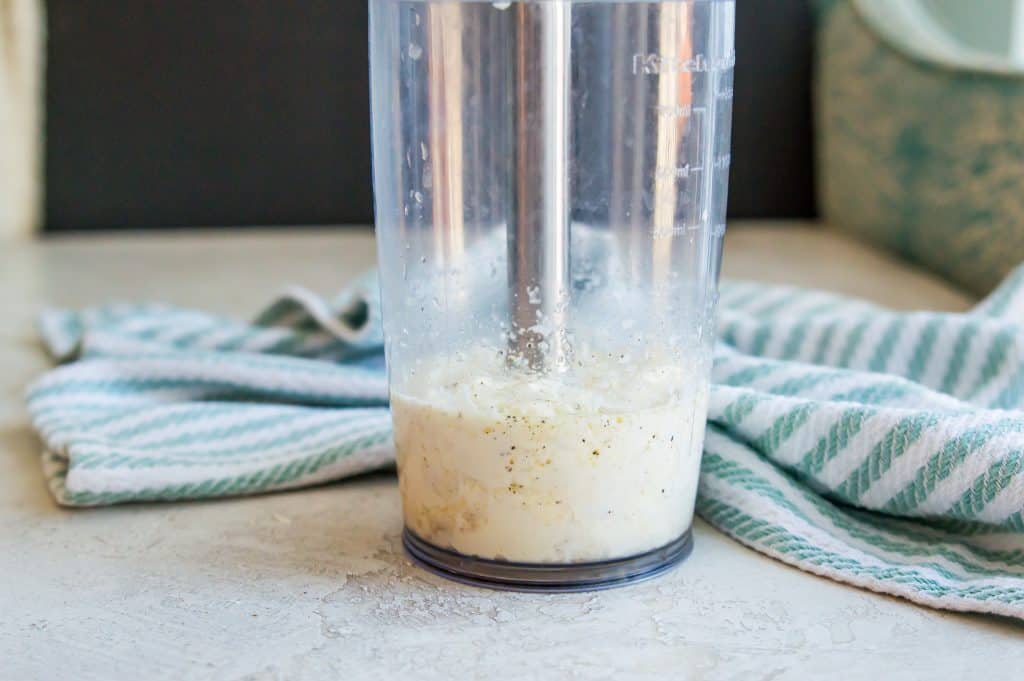 An immersion blender cup filled with ingredients for making aioli.