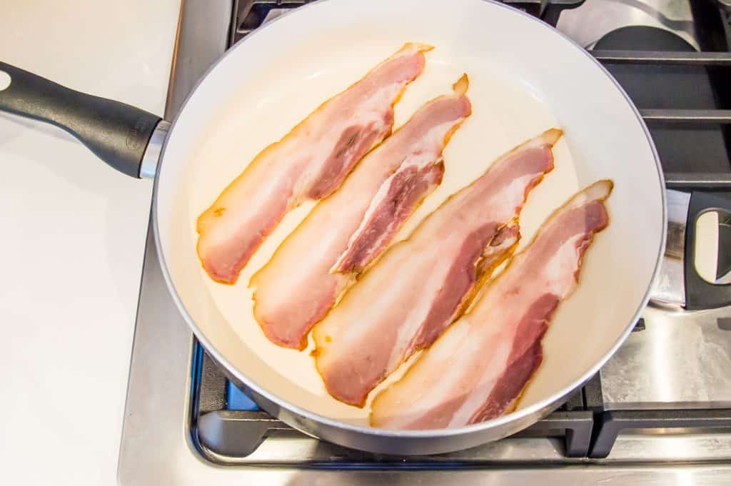 Bacon cooking in a pan on the stovetop.