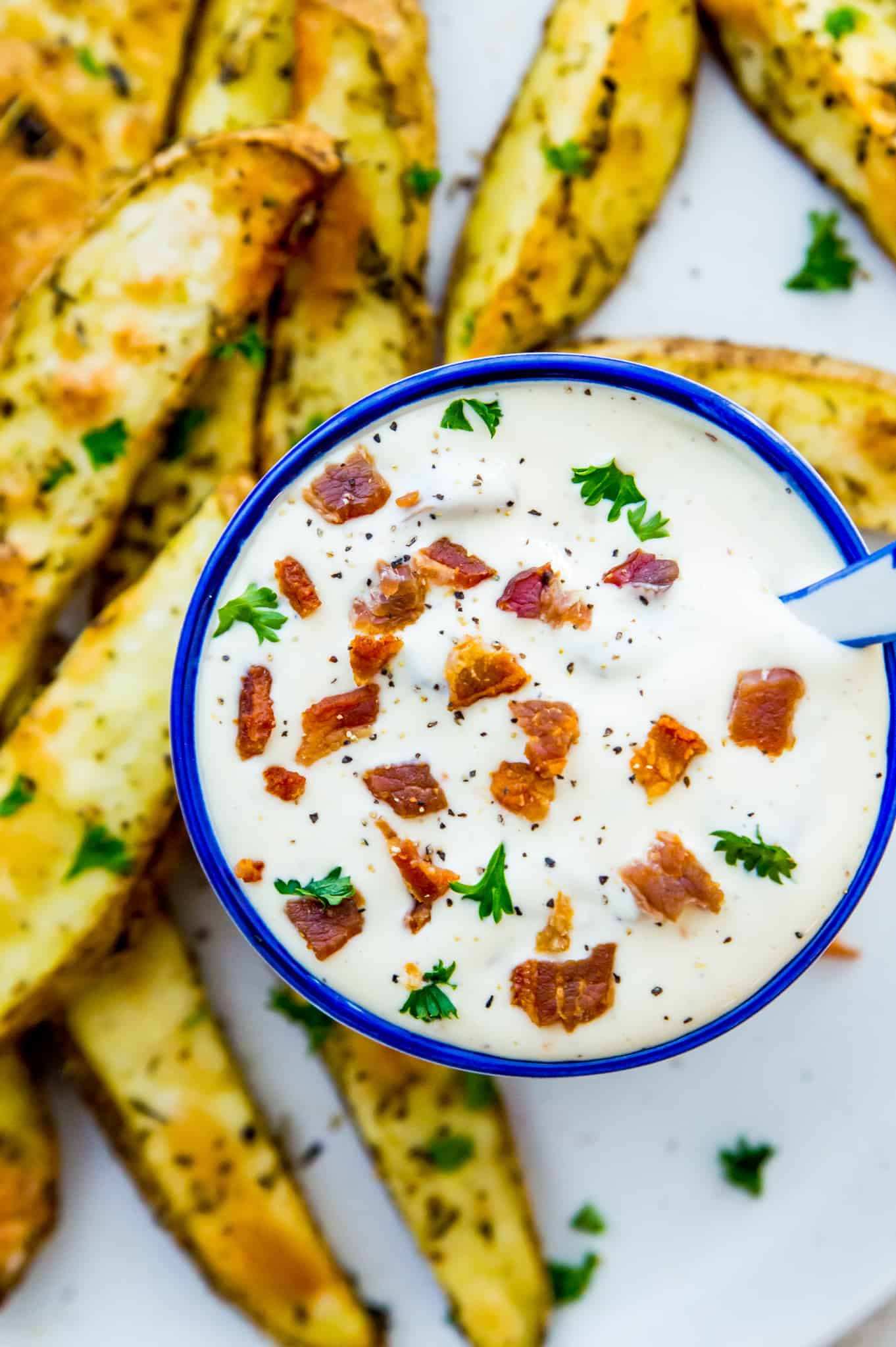 Aioli in a bowl with bacon pieces and parsley on top as garnish.