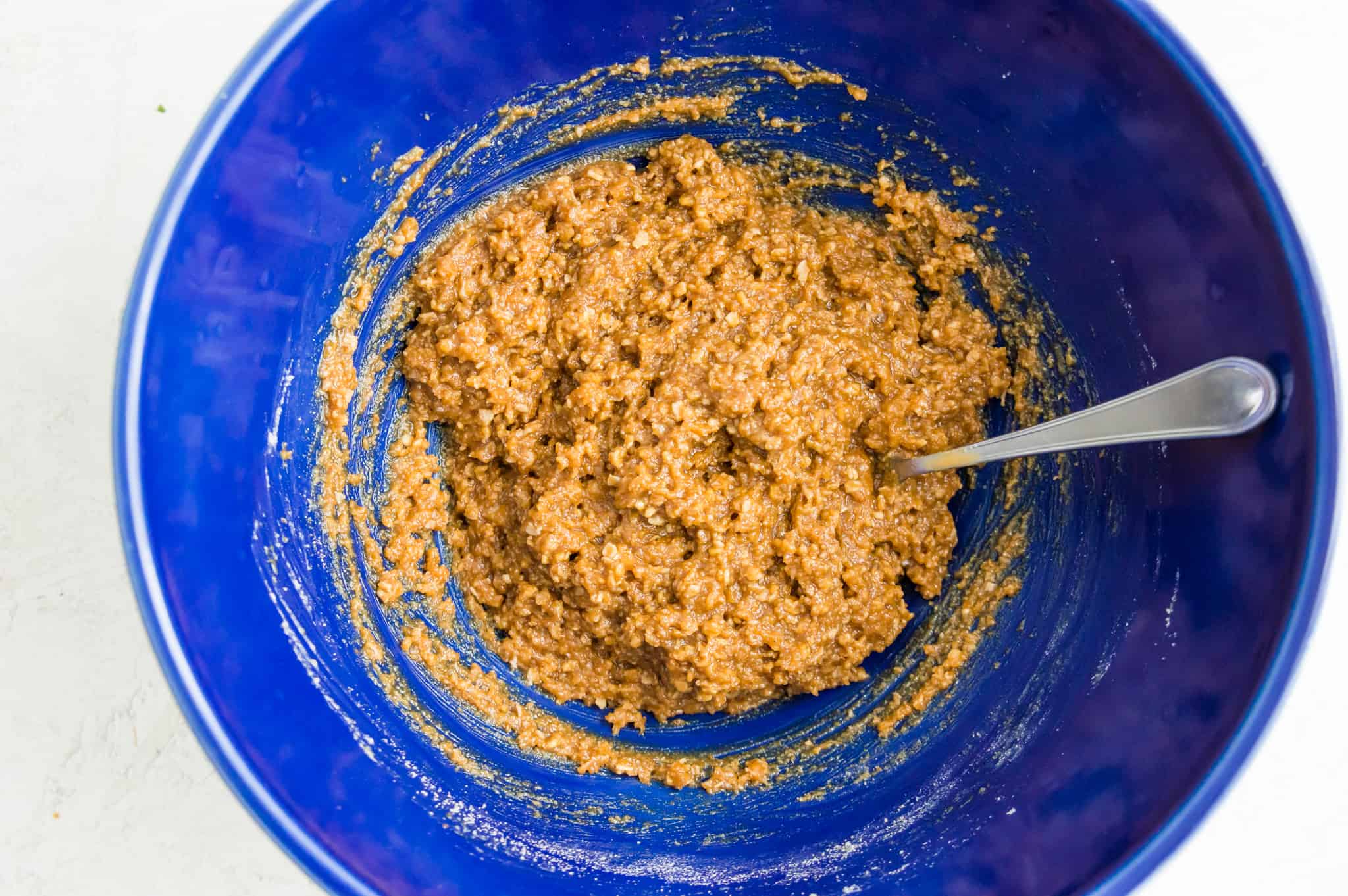 A large bowl with peanut butter cookie dough batter in it with a spoon in the batter.