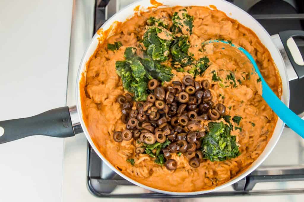 A pan full of sun dried tomato pasta with spinach and black olives on top.