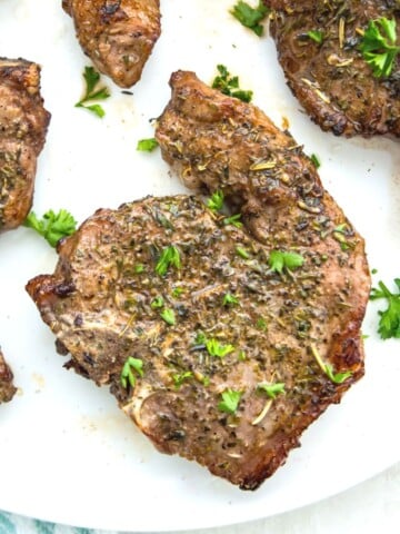 Cooked lamb chops on a plate, garnished with fresh parsley.