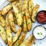 A plate of air fryer potato wedges with a side of ketchup and mayonnaise.