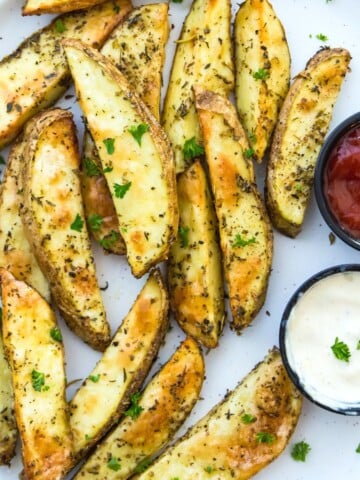 A plate of air fryer potato wedges with a side of ketchup and mayonnaise.