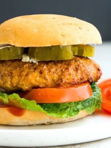 A turkey burger on a plate in a bun with lettuce, tomato and pickles.