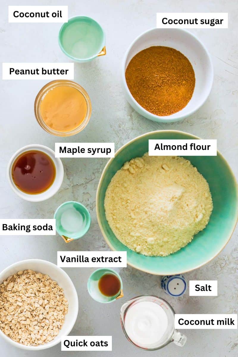 The ingredients needed to make vegan peanut butter oatmeal cookies separated into bowls including peanut butter, almond flour, maple syrup and coconut oil.