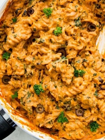 A pan filled with vegan sun-dried tomato pasta with a serving spoon in it.