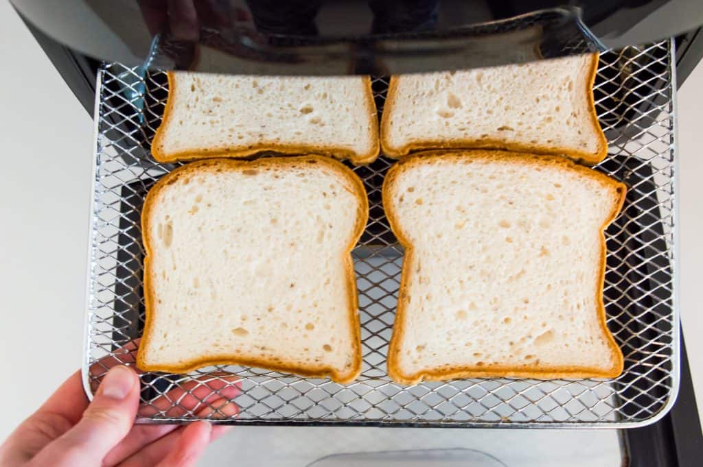 Four pieces of bread on an air fryer tray.