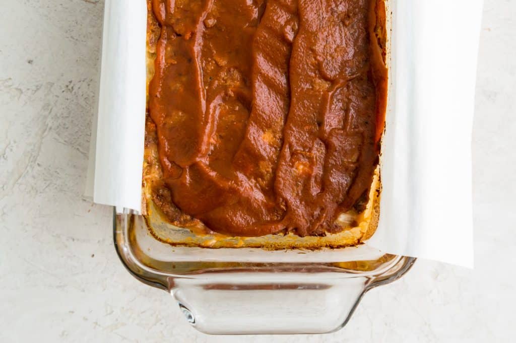 A meatloaf in a bread pan topped with barbecue sauce. 