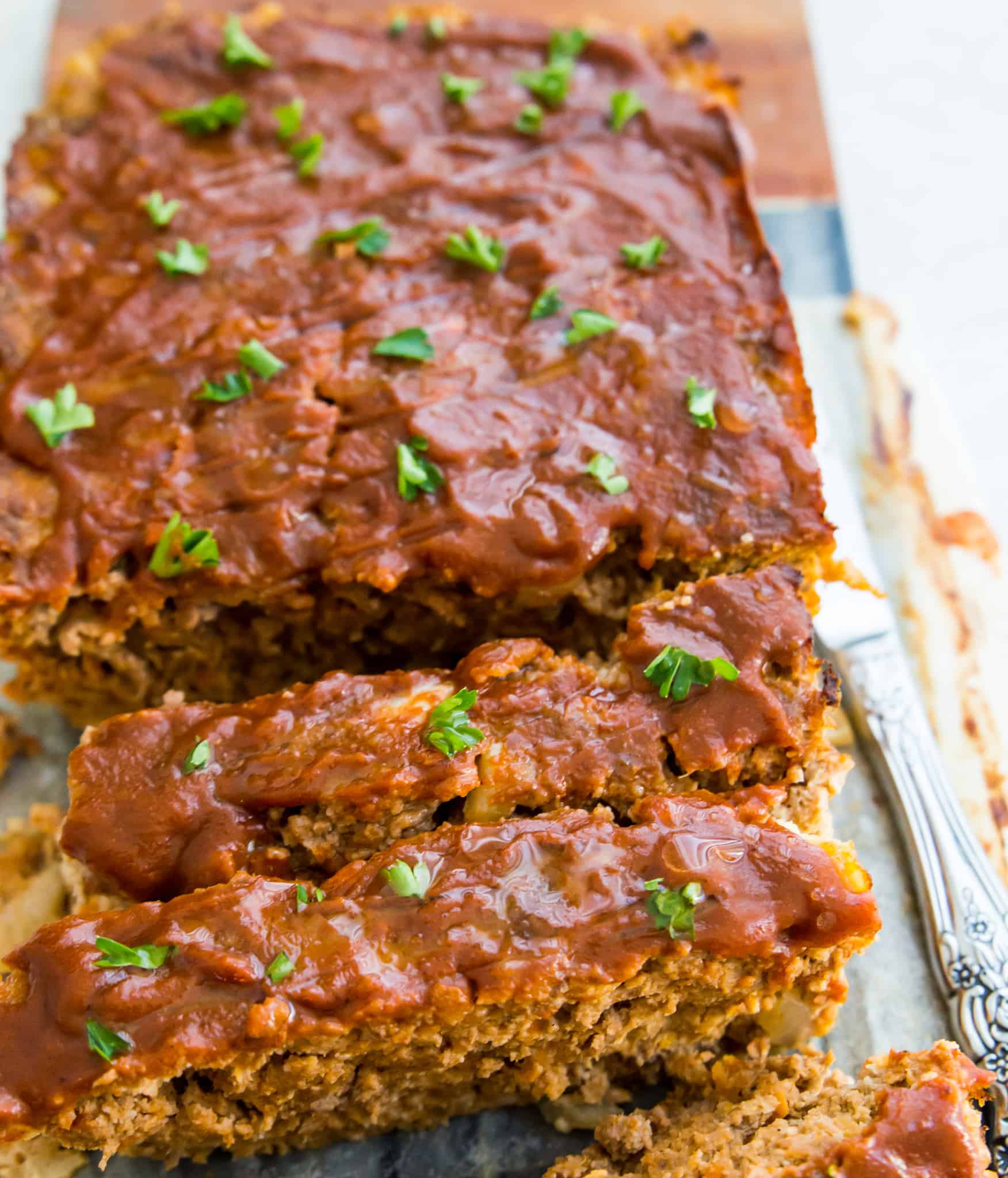 A gluten free meatloaf with bbq sauce on top, cut up on a platter.