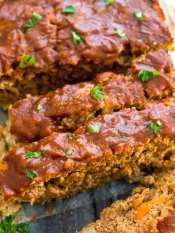 A loaf of gluten free meatloaf cut into pieces and garnished with fresh parsley.