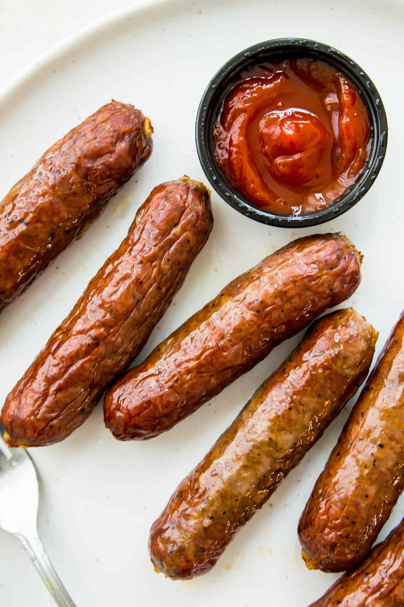 Sausages cooked in an air fryer on a plate with ketchup.