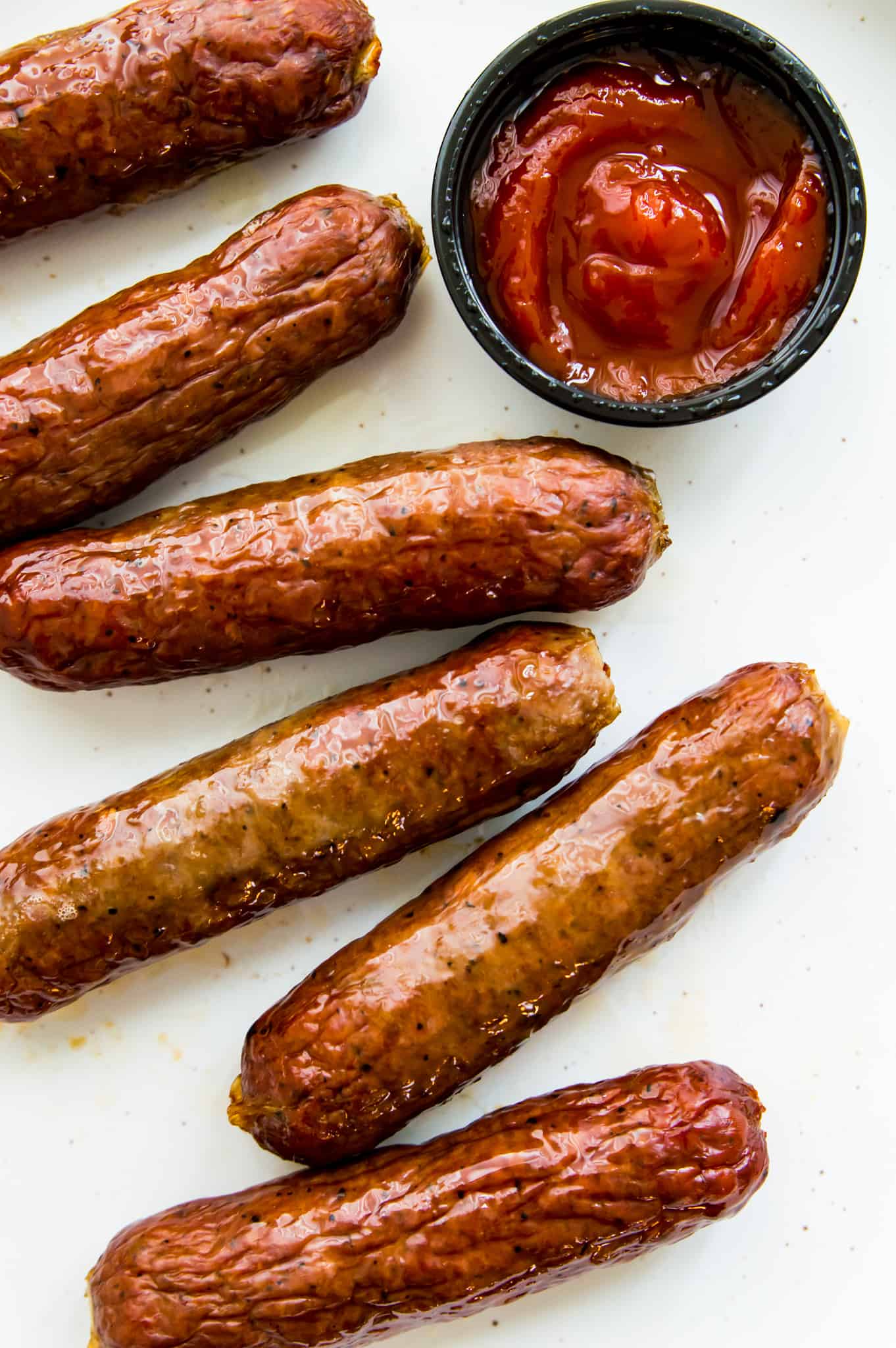 A plate with cooked Italian sausages on it with a side of ketchup.