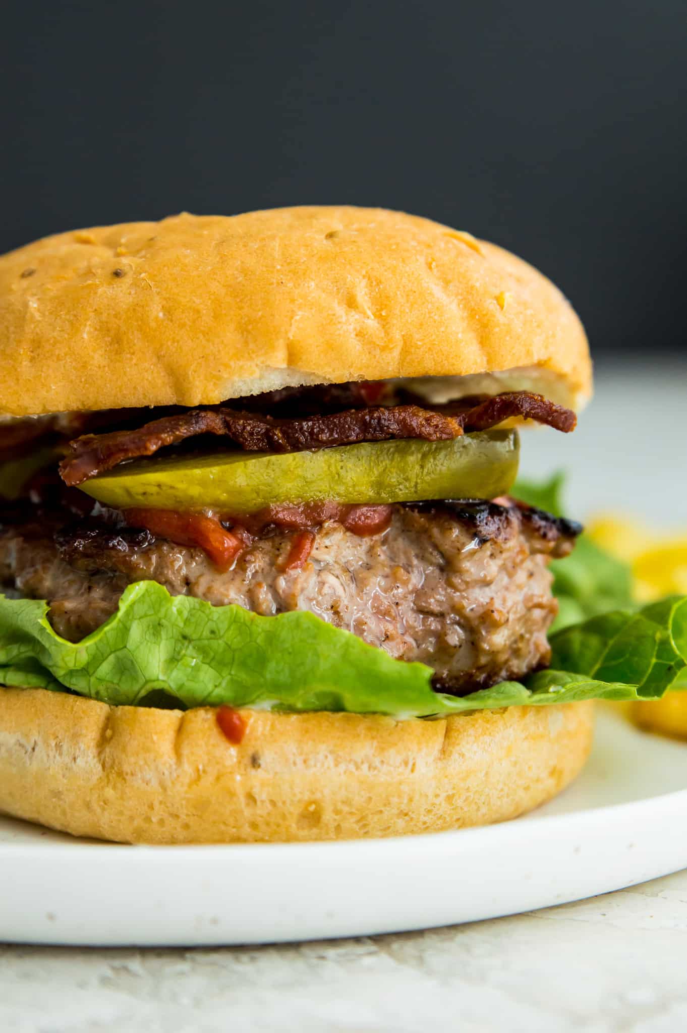 A homemade duck burger in a bun with lettuce, pickles, bacon and ketchup. 