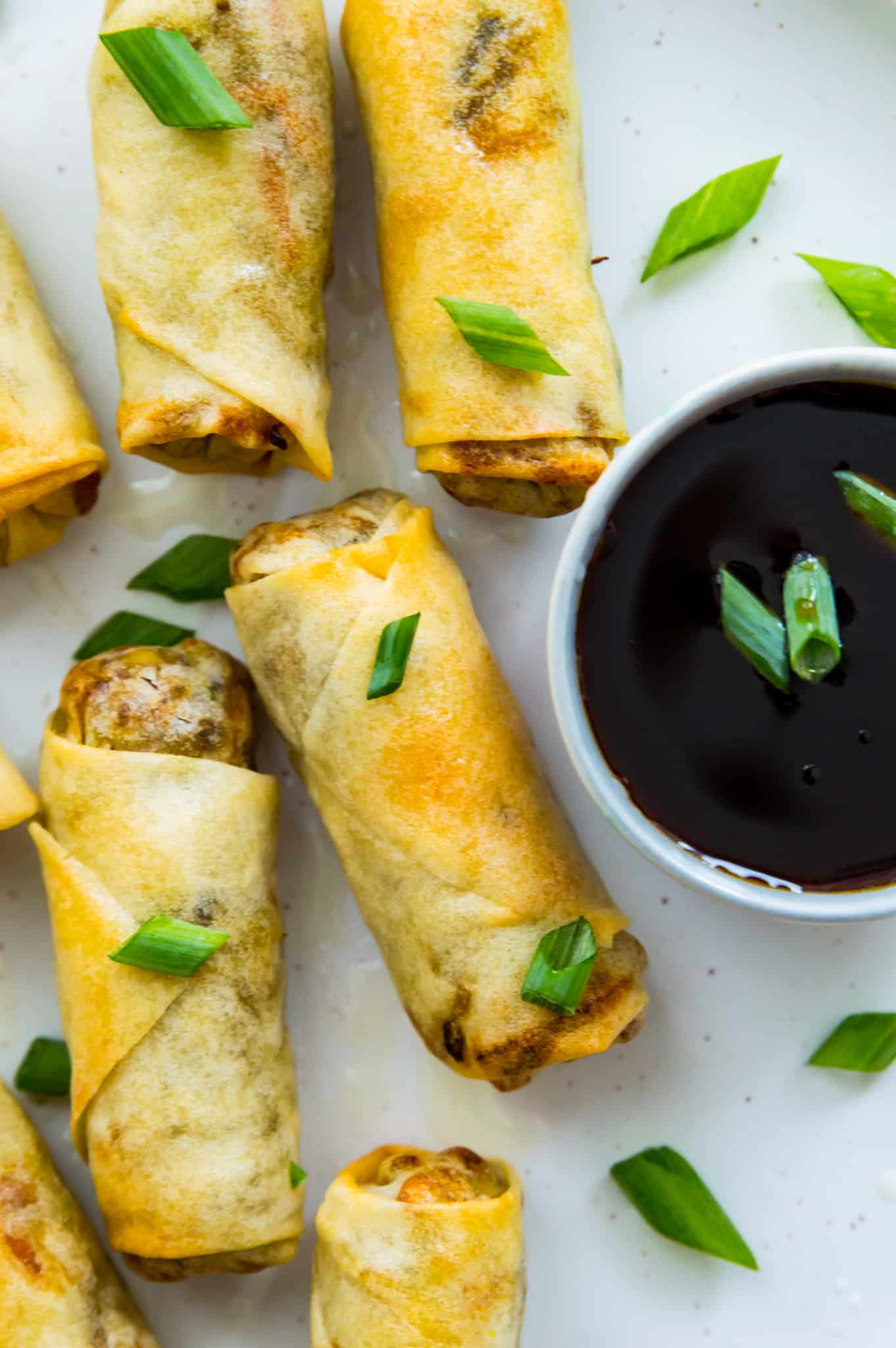Egg rolls cooked in an air fryer on a plate with a dish of soy sauce. 