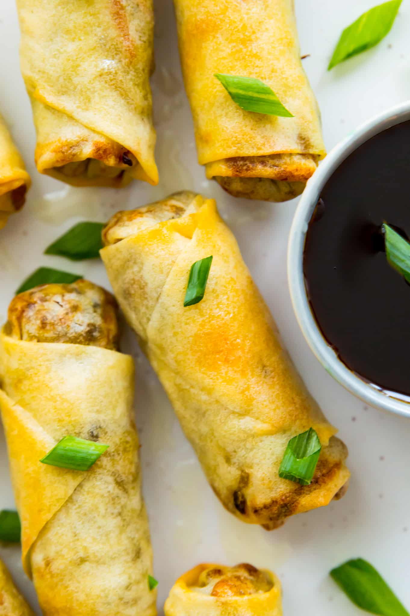 Egg rolls on a plate with a dish of soy sauce and garnished with green onion.
