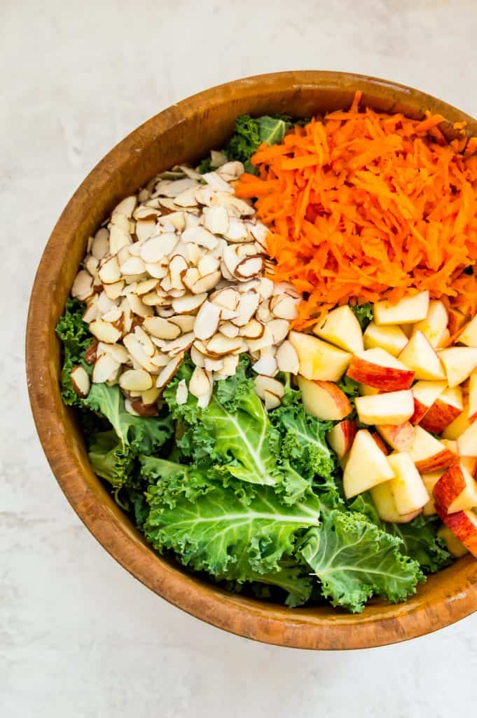 Ripped kale, sliced apples, shredded carrots and slivered almonds in a wooden salad bowl.
