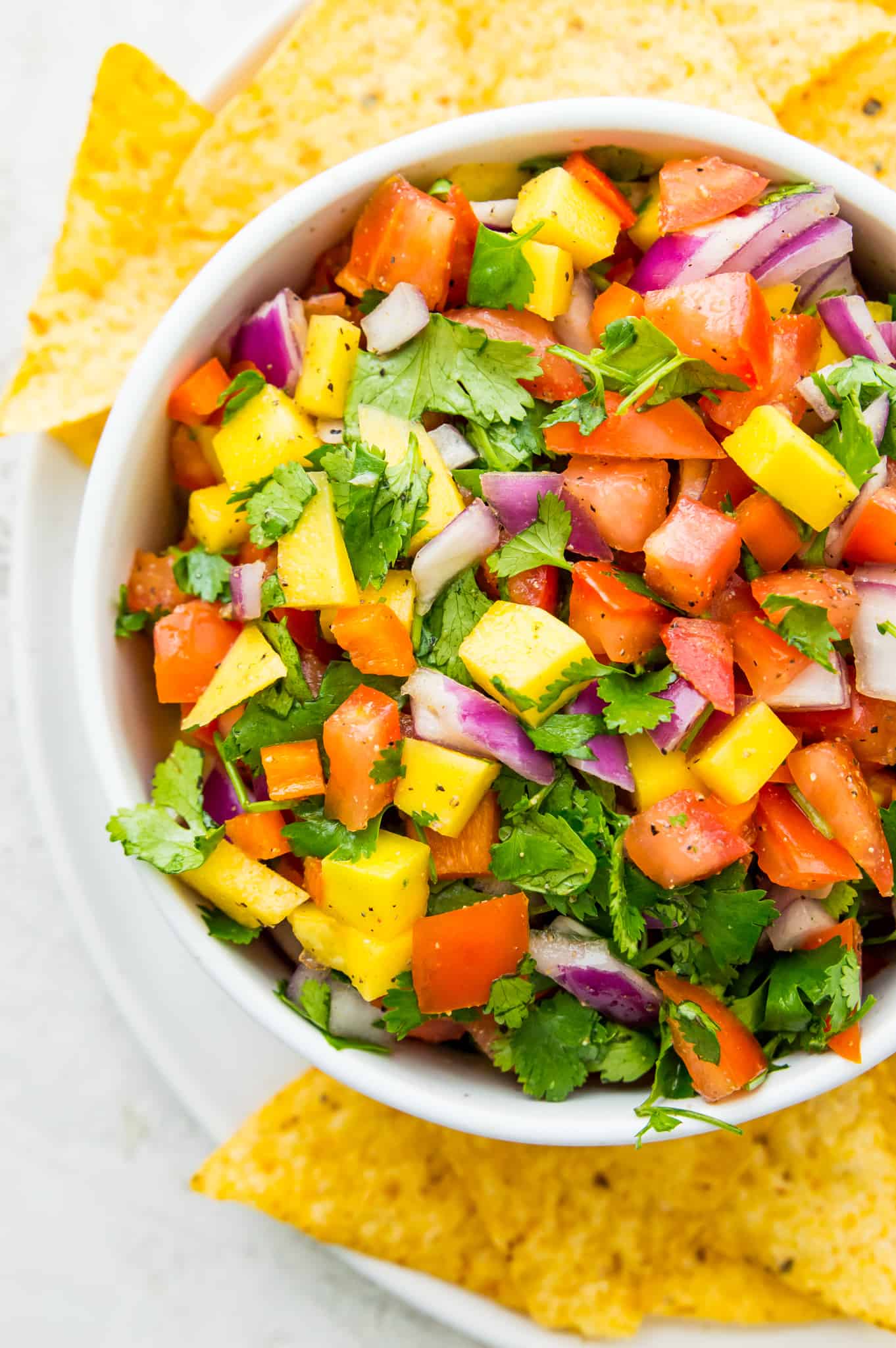 A bowl of mango habanero salsa with red onion, tomatoes, cilantro, and pepper.