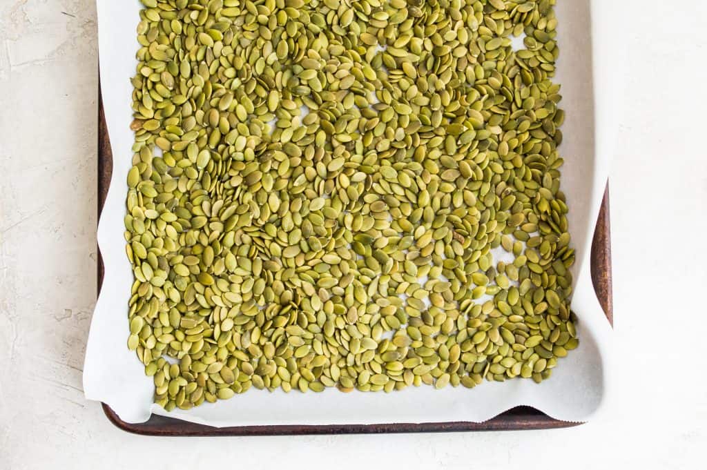 Raw pumpkin seeds on a baking sheet lined with parchment paper. 
