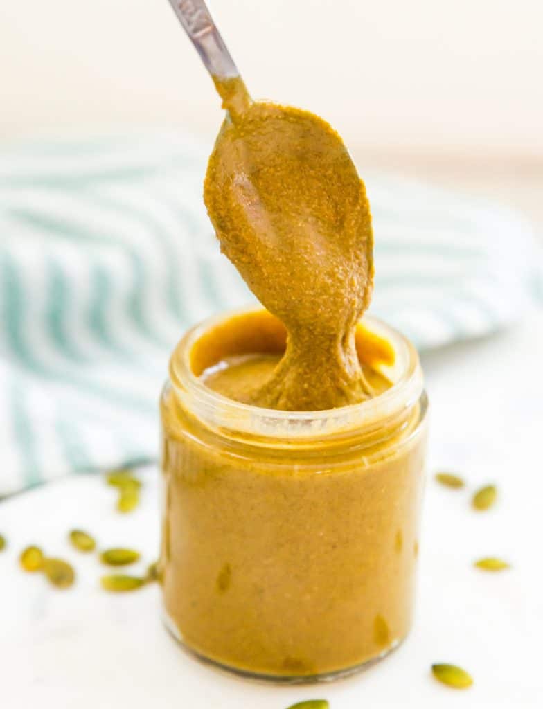 A jar of homemade pumpkin seed butter with a spoon in it