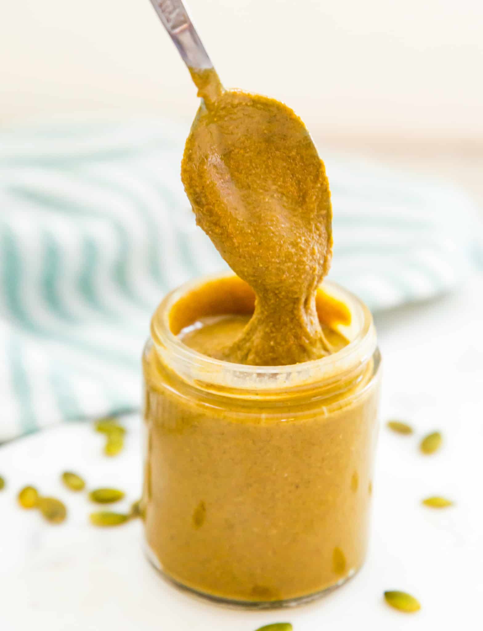 A jar of homemade pumpkin seed butter with a spoon in it.