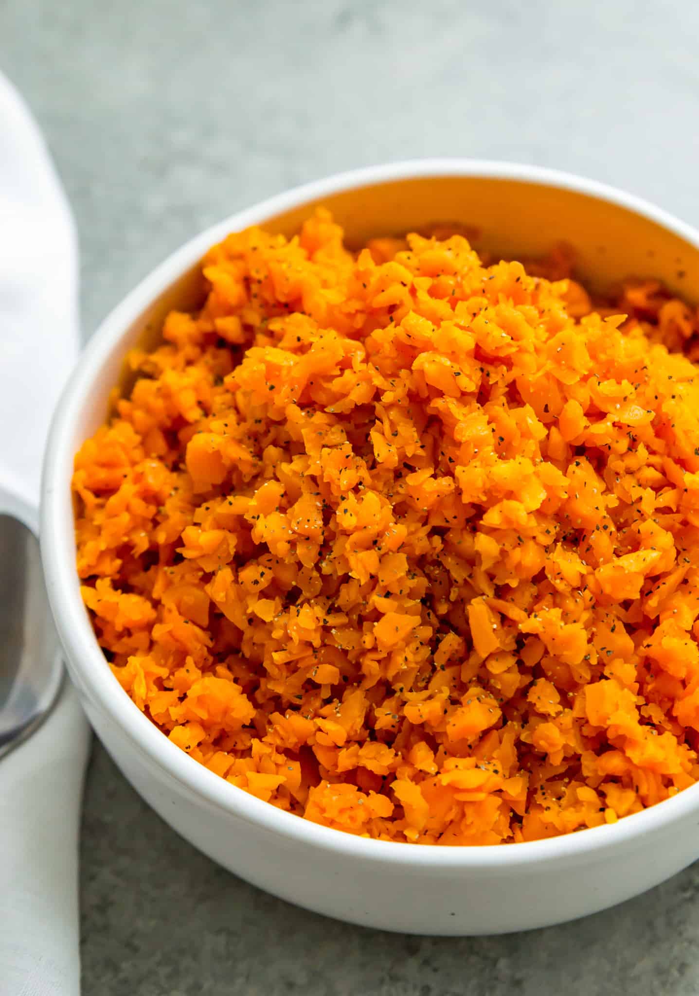 A white bowl filled with riced sweet potatoes with salt and pepper on top for garnish. 