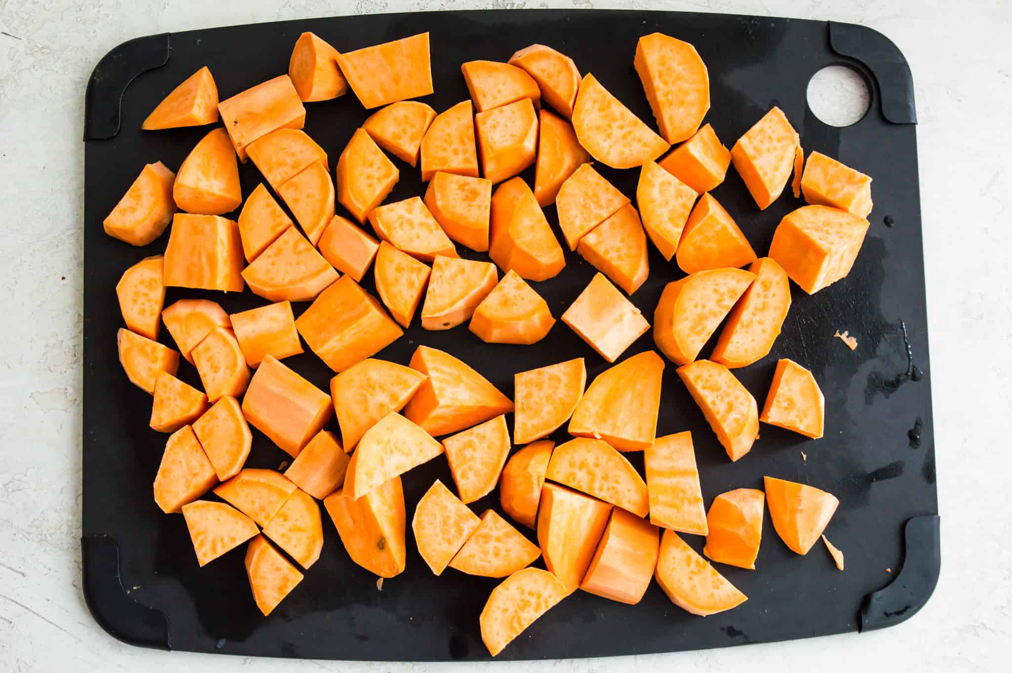 A black cutting board with peeled and chopped sweet potatoes on it.