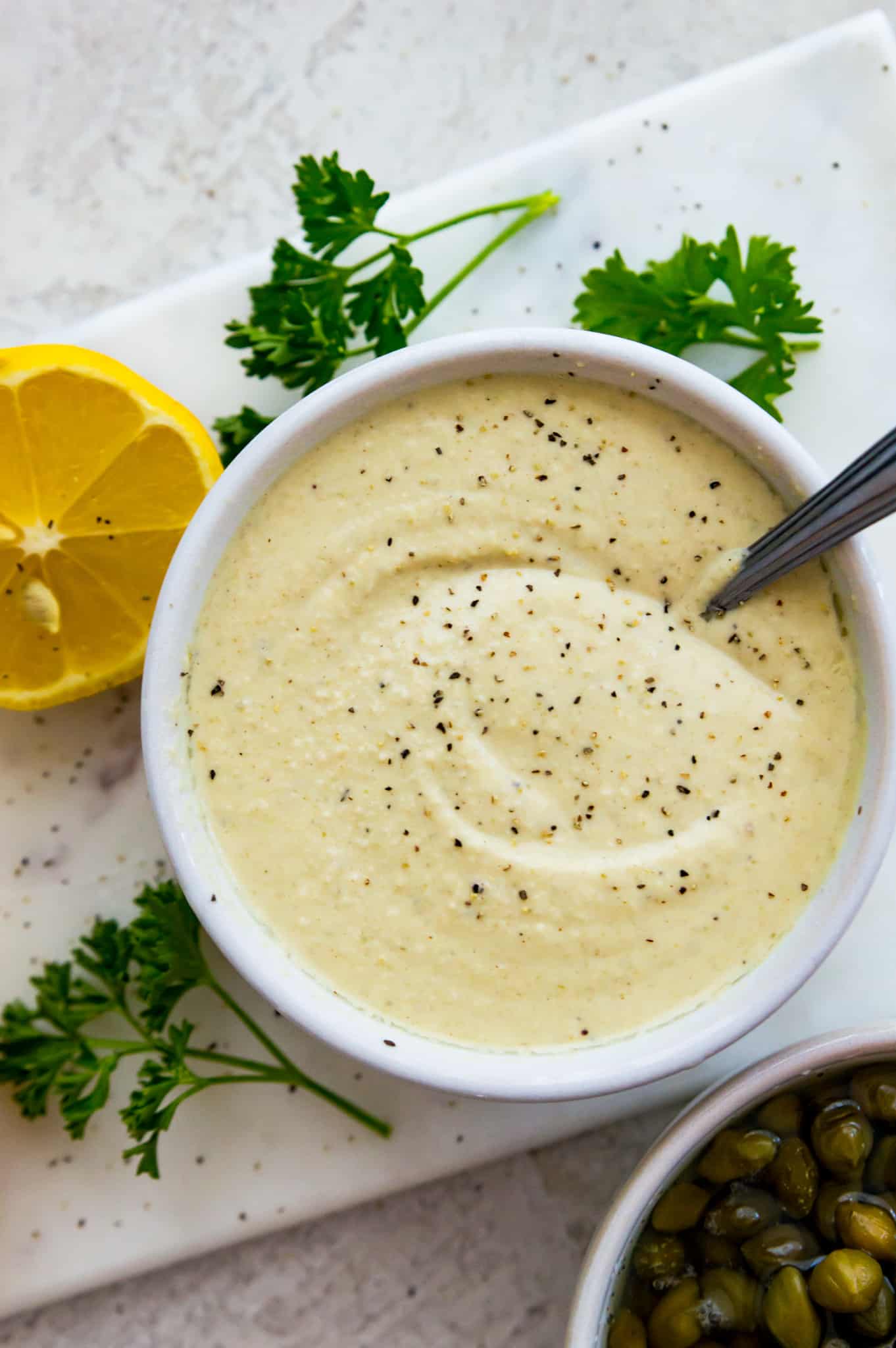 A Caesar salad dressing a bowl surrounded by fresh parsley. 