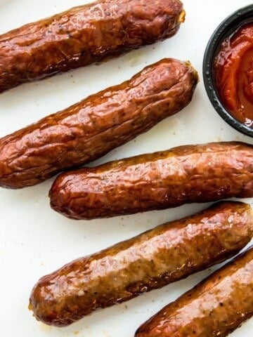 A plate of cooked Italian sausages with a side of ketchup.